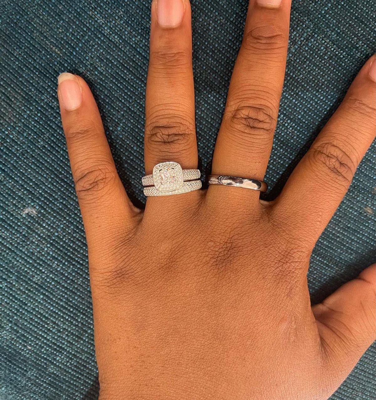 Diamond engagement ring and wedding band on a hand against teal fabric
