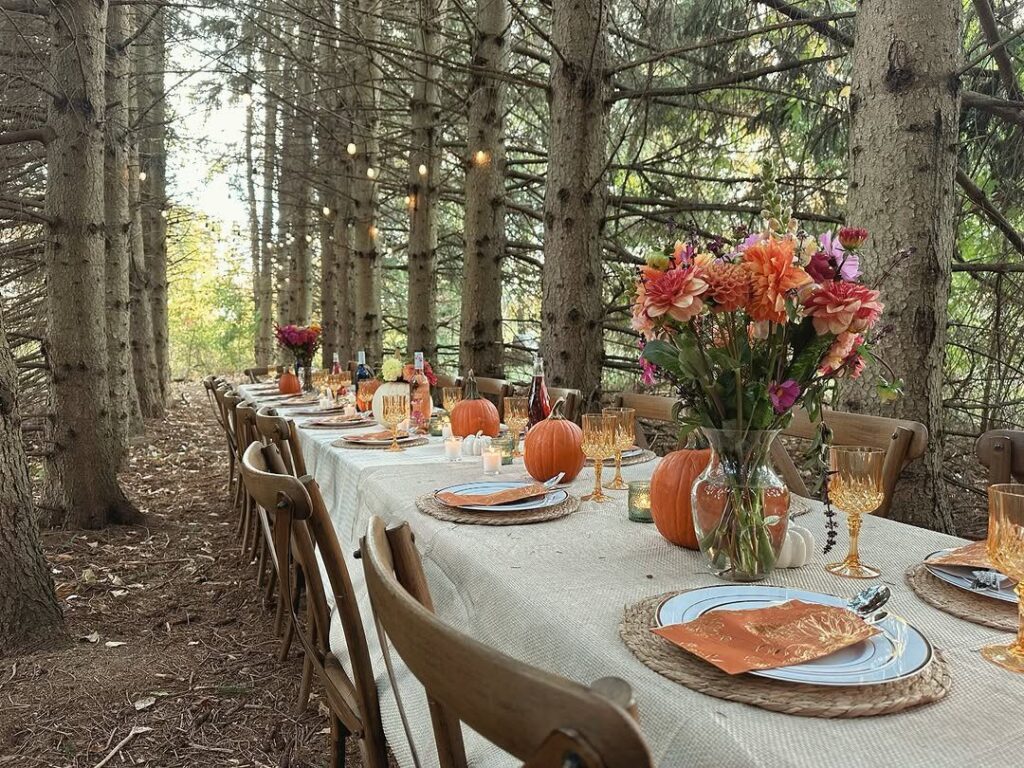 Long dining table set with pumpkins and flowers in a pine forest setting.