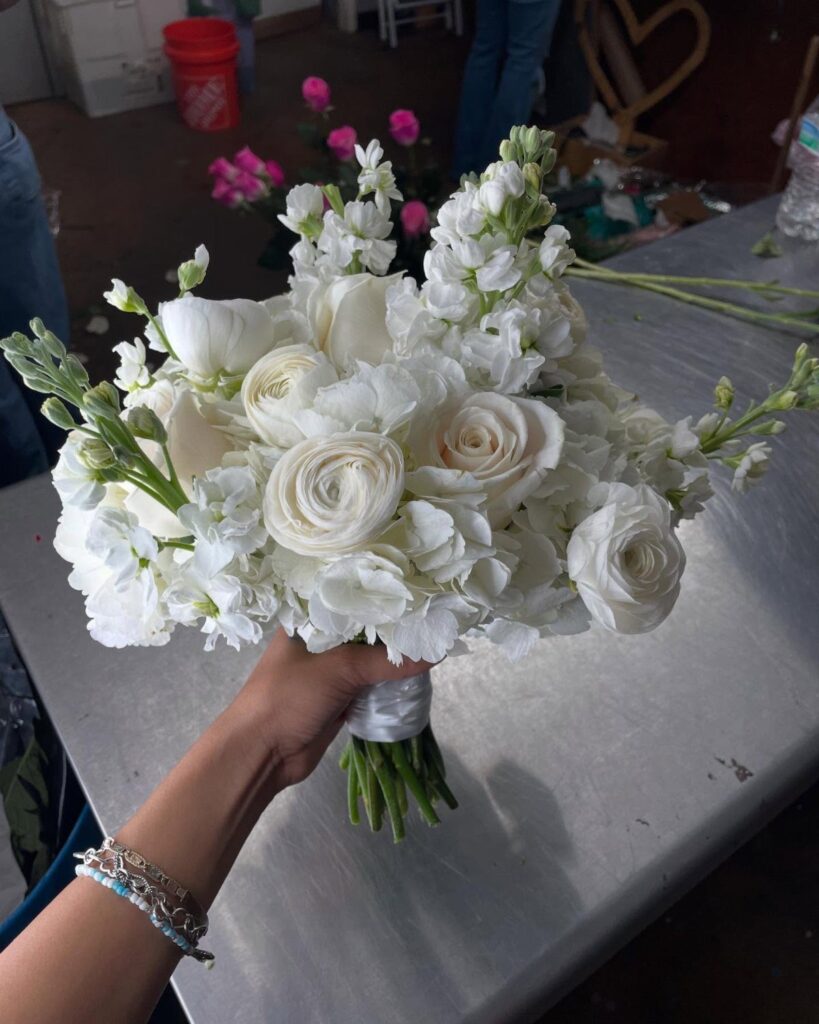White wedding bouquet with roses and ranunculus held by a hand over a table