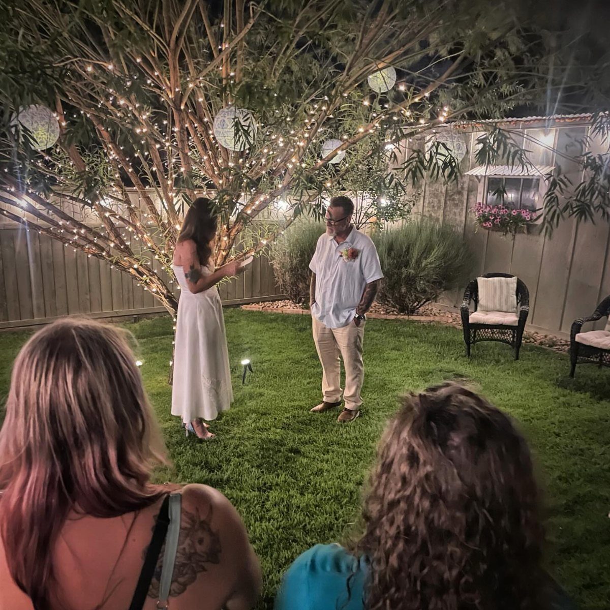 Couple exchanging vows in a backyard at night under a tree with string lights.