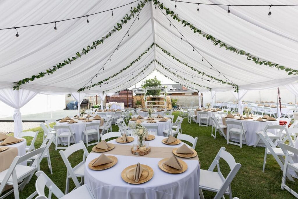 White wedding tent on a lawn with decorated round tables and string lights.
