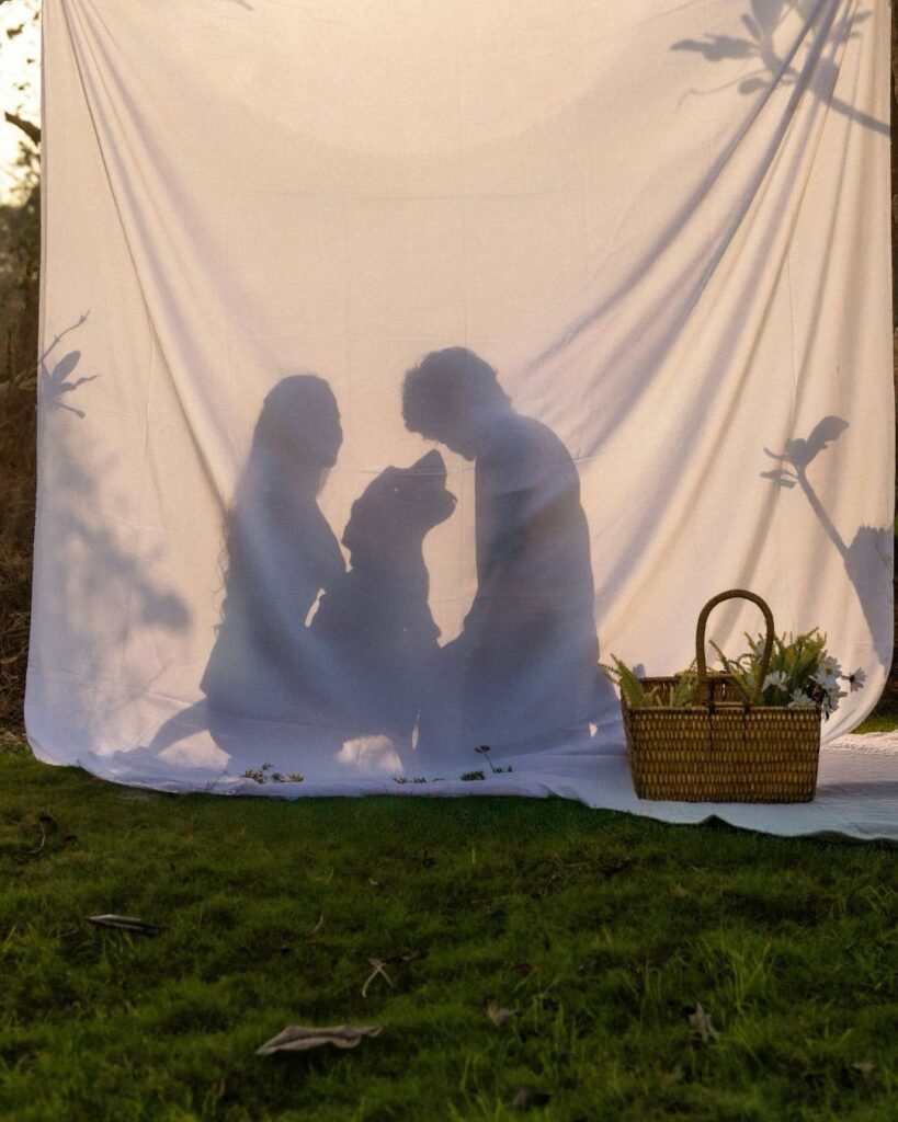 Couple and their dog silhouetted behind a white sheet with a flower basket.