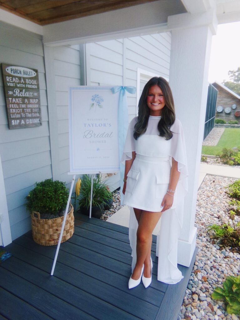 Woman in a short white bridal shower dress with a sheer cape overlay.