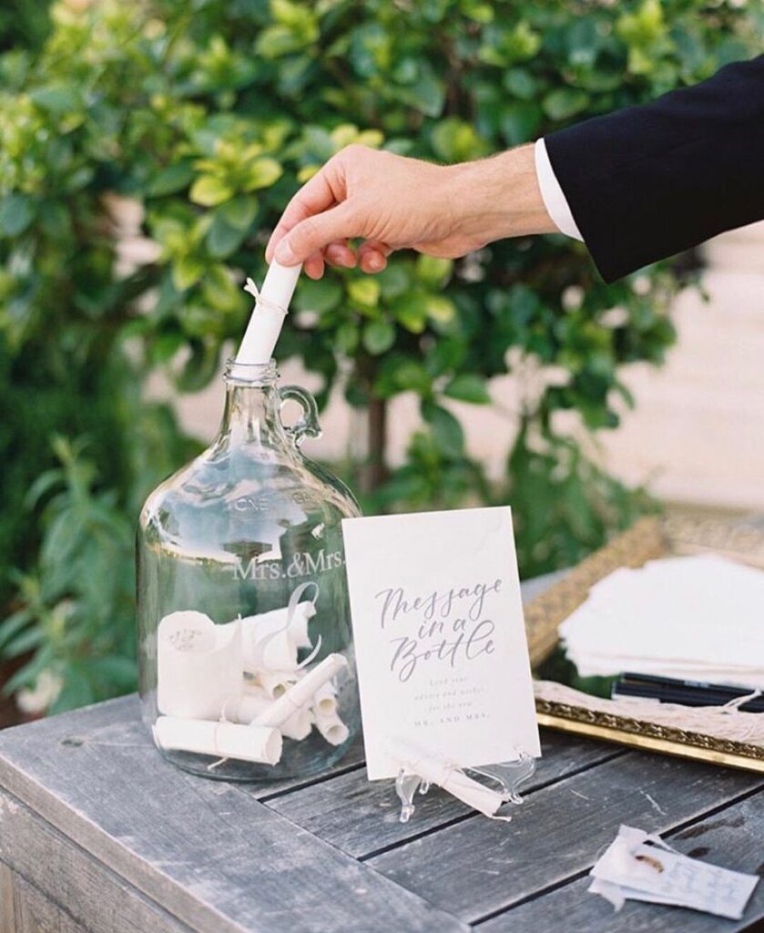 Hand placing a rolled note into a glass bottle for a guest book.