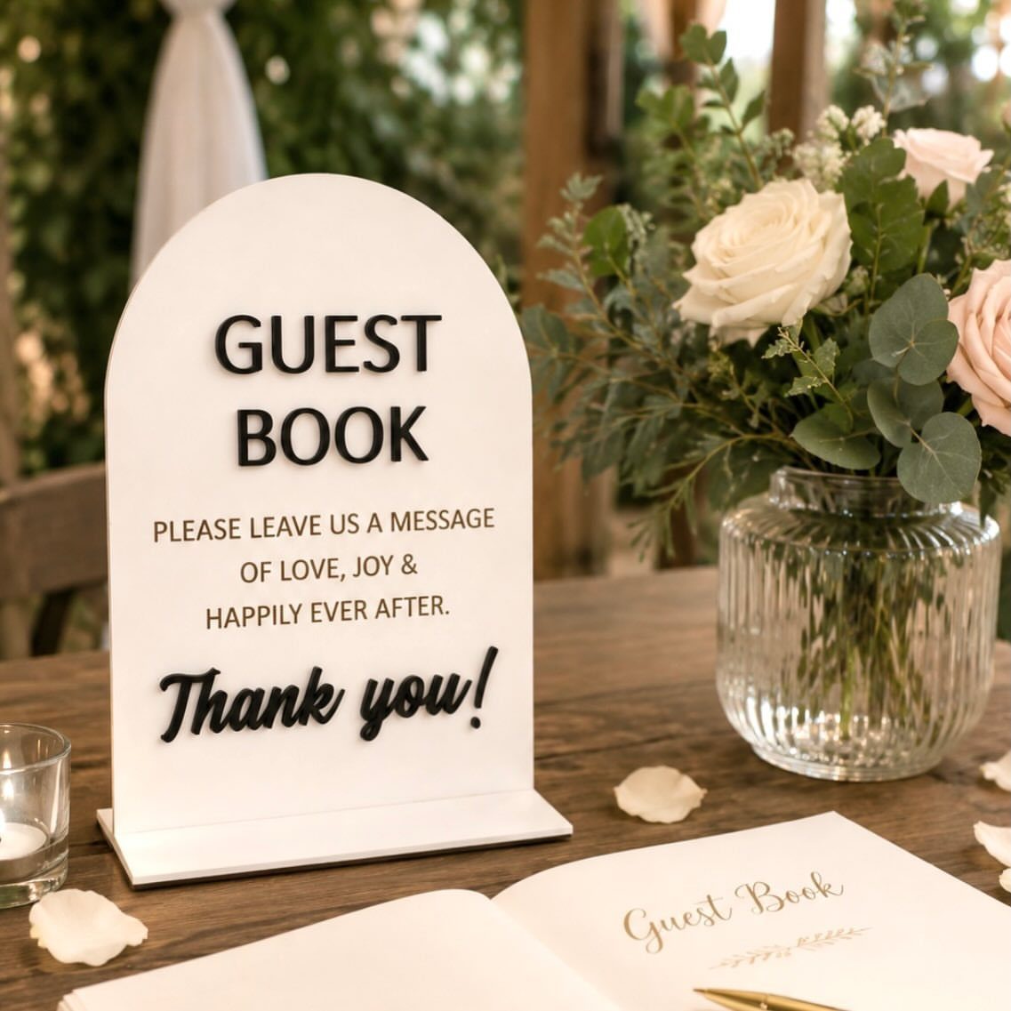 Arched white guest book sign on a wooden table with white roses.