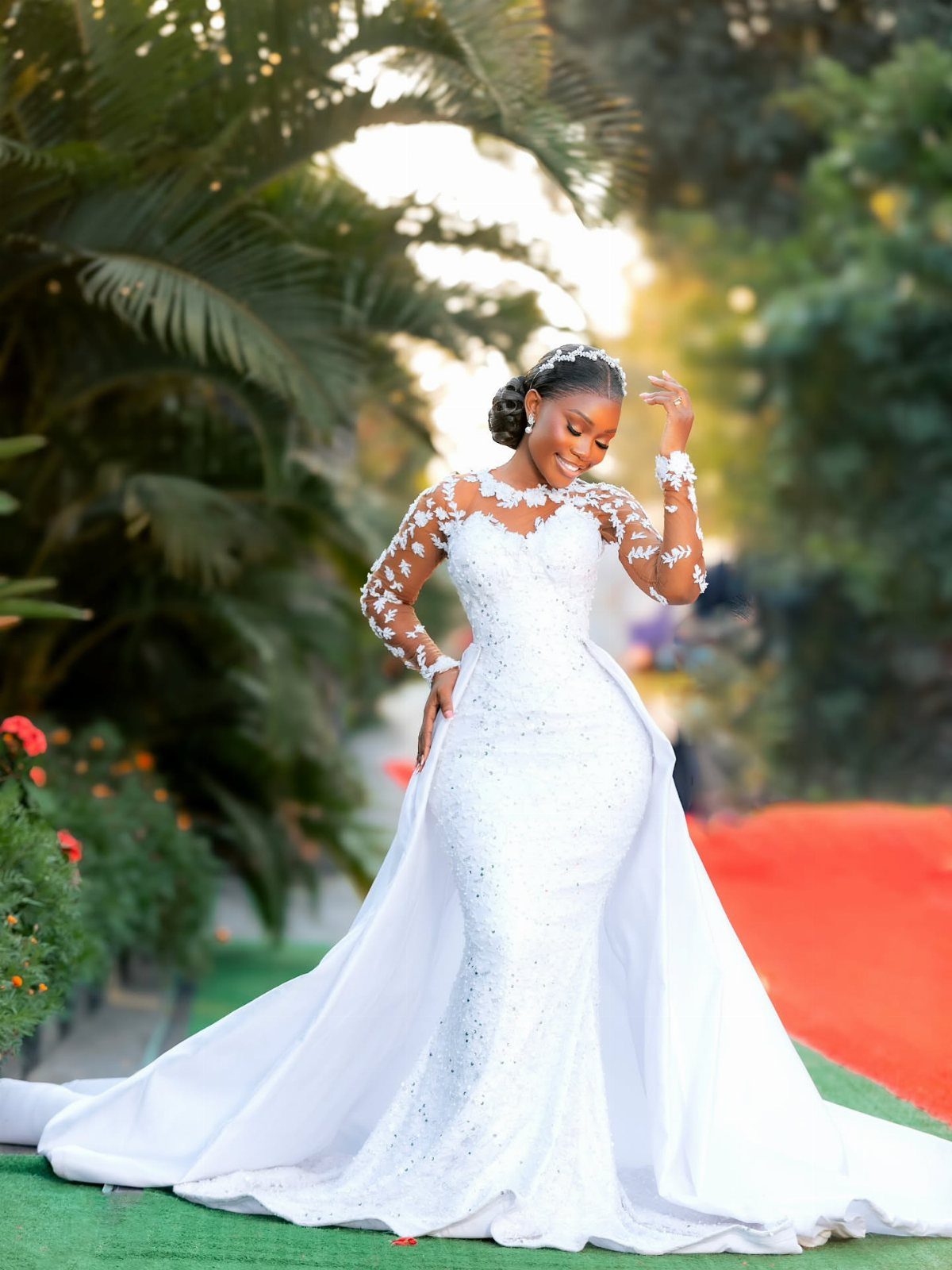 Woman in a white lace wedding gown with a long train outdoors.