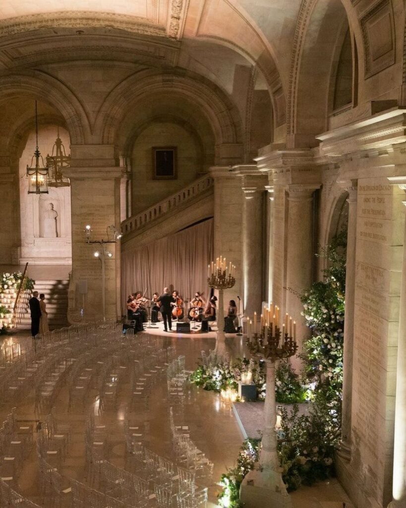 Wedding ceremony setup in a grand stone hall with ghost chairs and orchestra