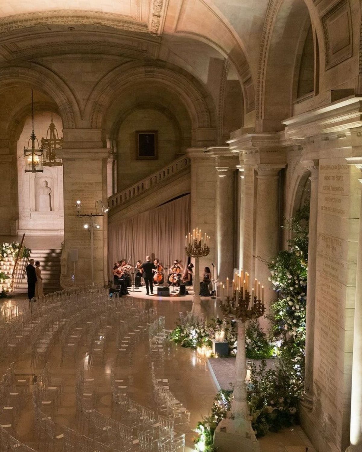 Wedding ceremony setup in a grand stone hall with ghost chairs and orchestra