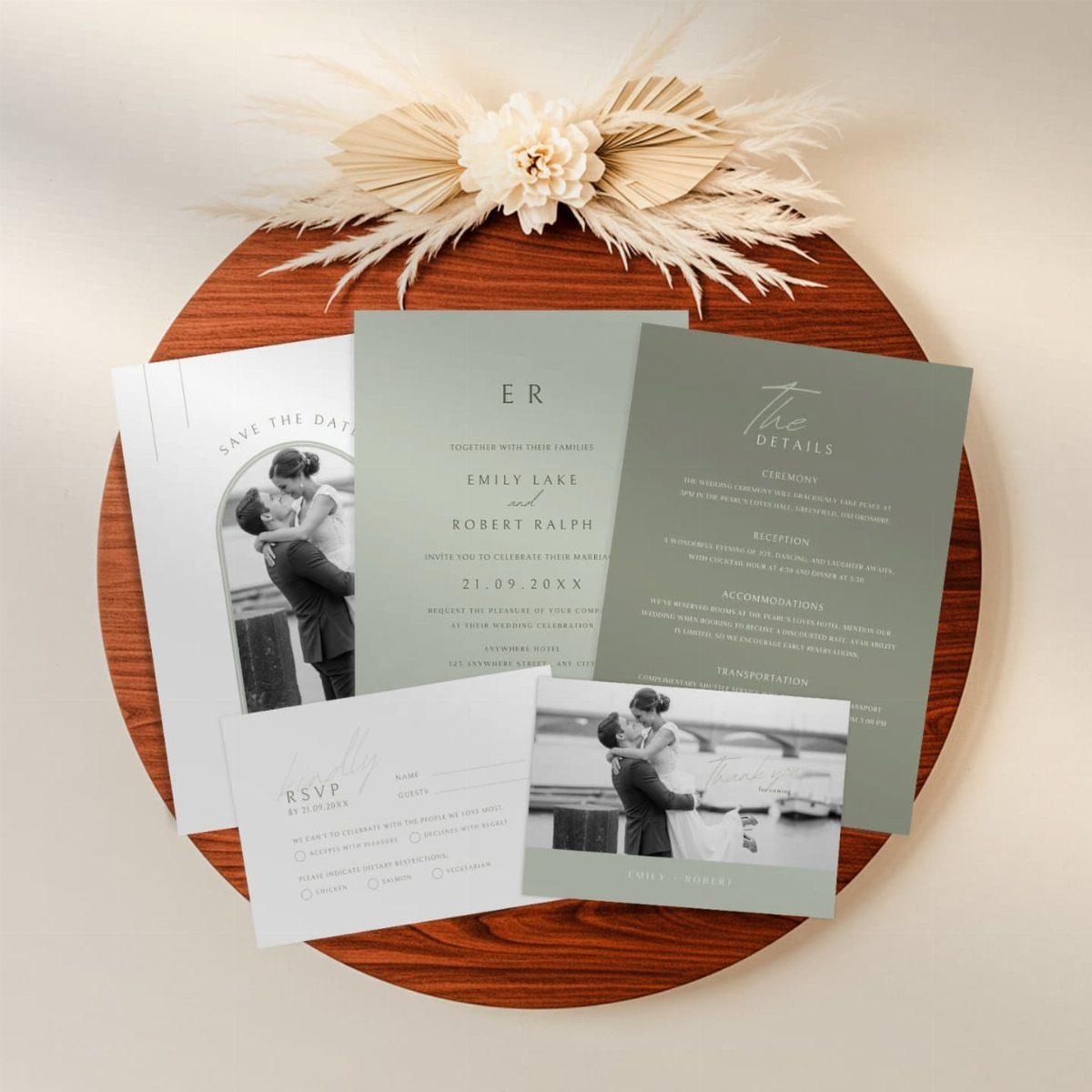 Sage green and white wedding invitation suite arranged on a wooden tray with dried florals.