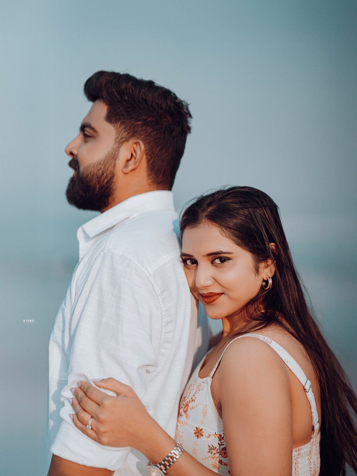 Couple posing back-to-back with the woman wearing a ring and floral dress.