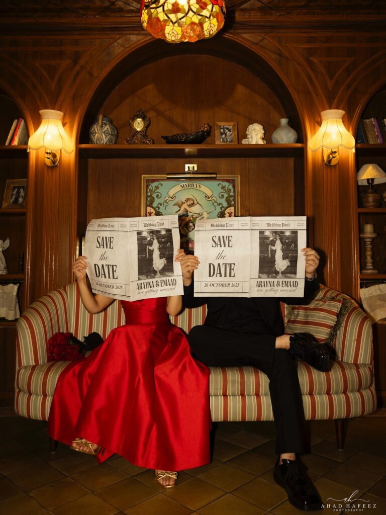 Couple in formal wear holding Save the Date signs over their faces on a sofa