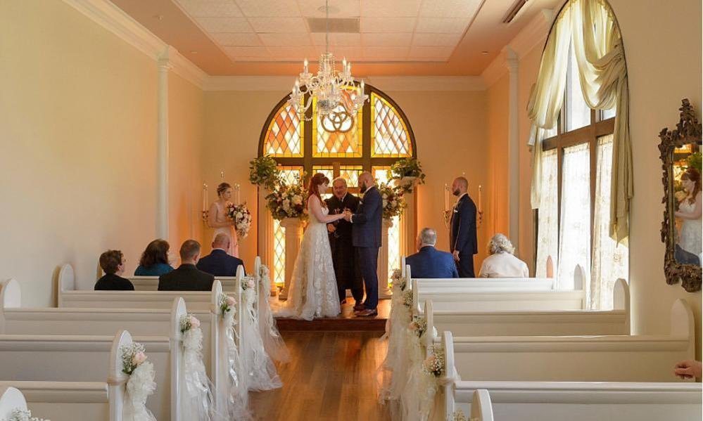 Bride and groom holding hands during a wedding ceremony in a bright chapel.