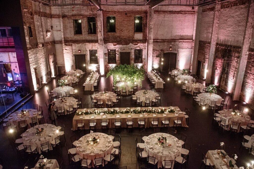 Industrial event space with exposed brick walls and white clothed wedding reception tables.