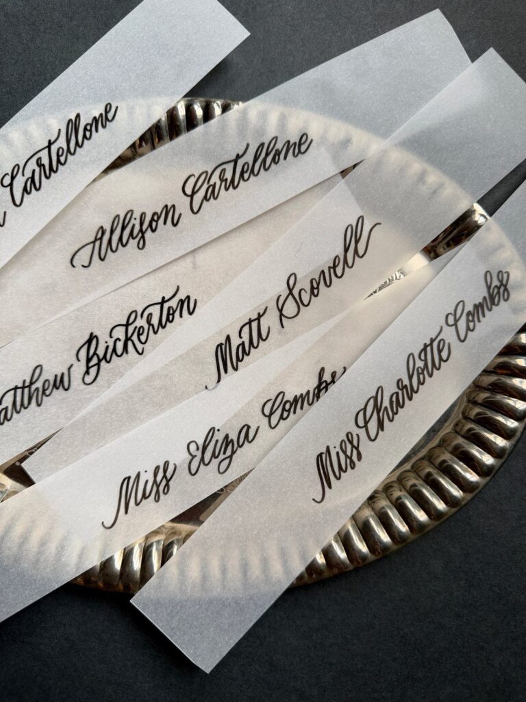 Translucent vellum paper strips with black calligraphy resting on a silver platter