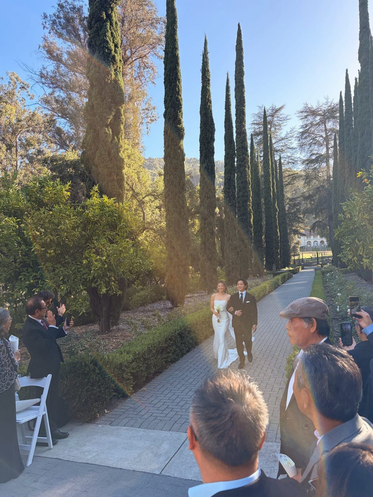 Bride in white gown walking down stone aisle escorted by a man