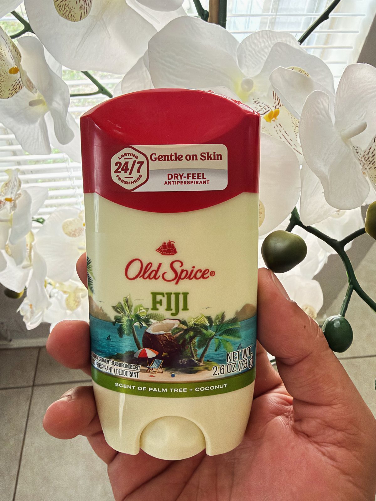 Old Spice Fiji antiperspirant deodorant held in a hand before white orchid flowers