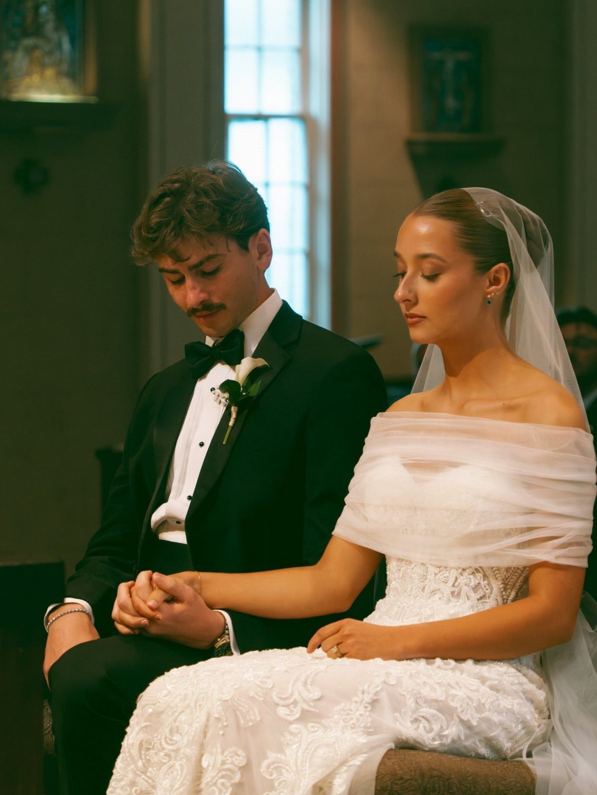 Bride and groom holding hands while sitting during a wedding ceremony in a church.