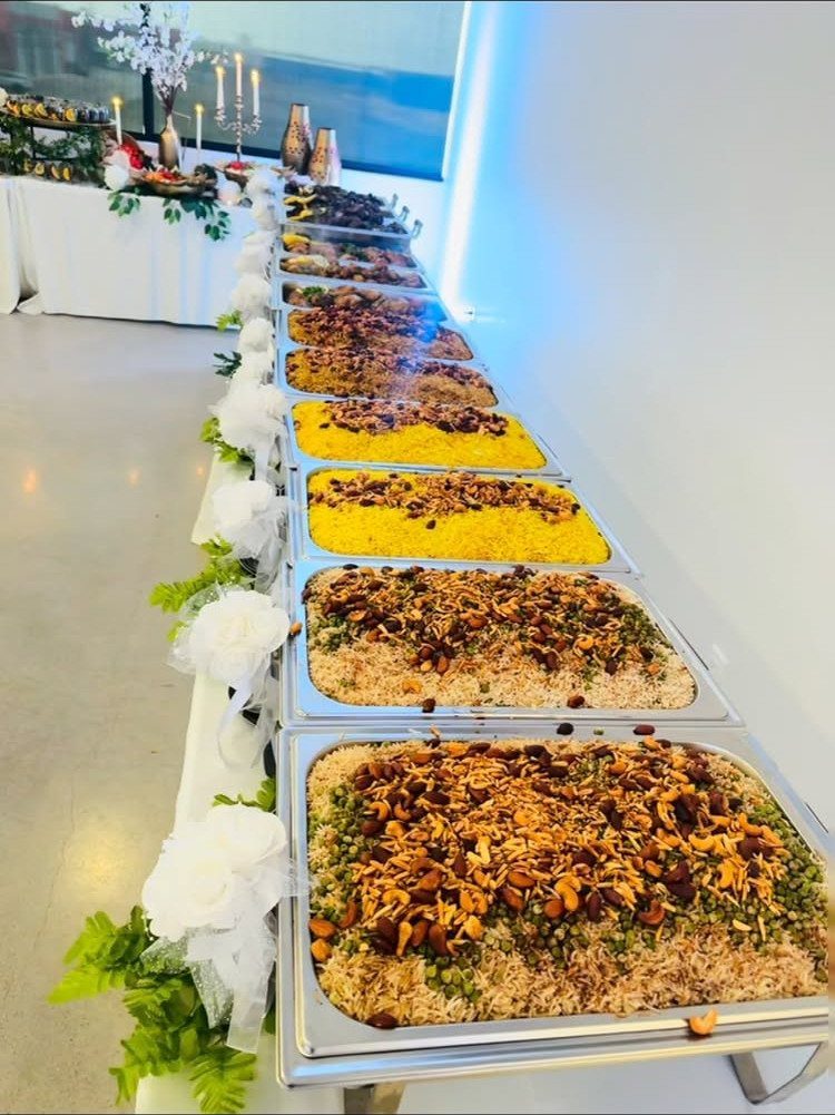 Buffet table with silver chafing dishes filled with rice and floral decorations.