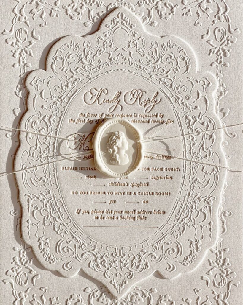 Ornate white embossed RSVP card with a wax seal and thin white string.