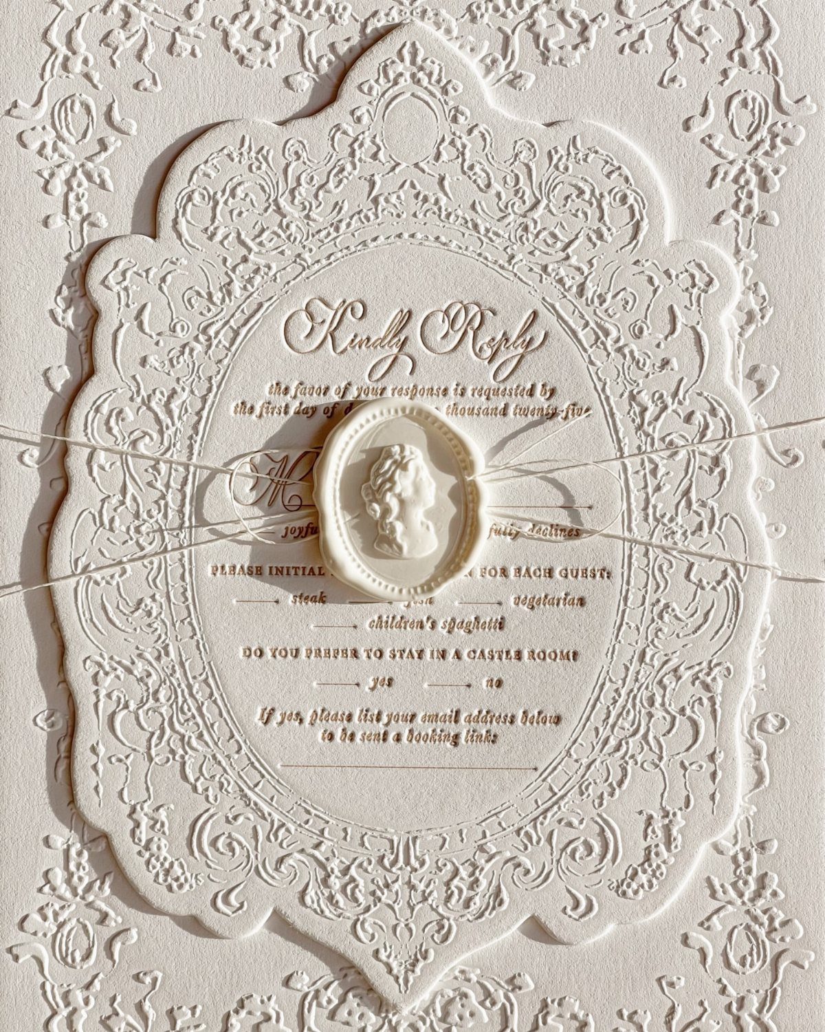Ornate white embossed RSVP card with a wax seal and thin white string.