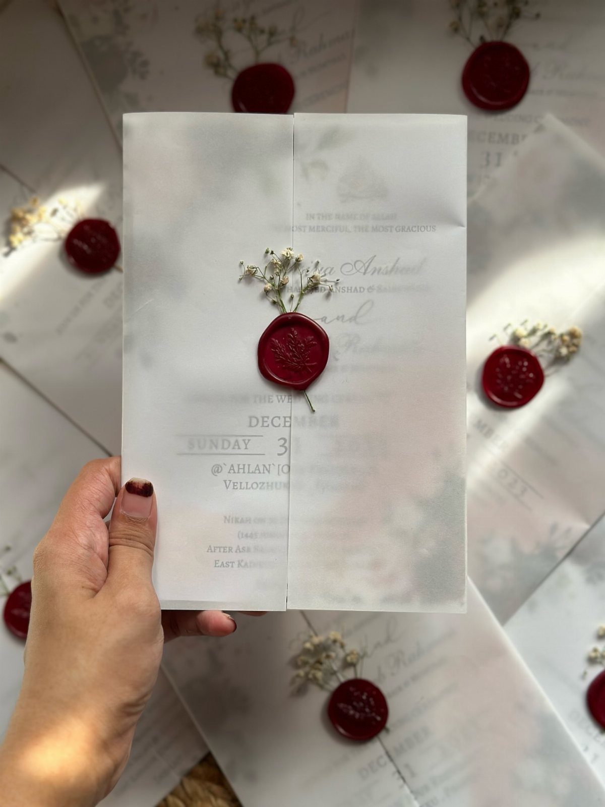 White wedding invitation card with a red wax seal and dried white flowers.