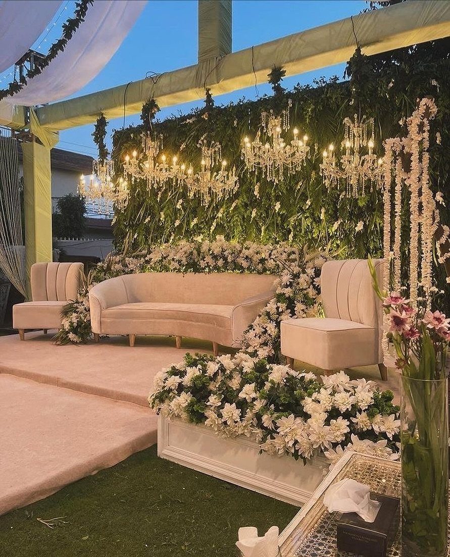 Elegant outdoor event seating with a beige sofa, green wall, and crystal chandeliers.