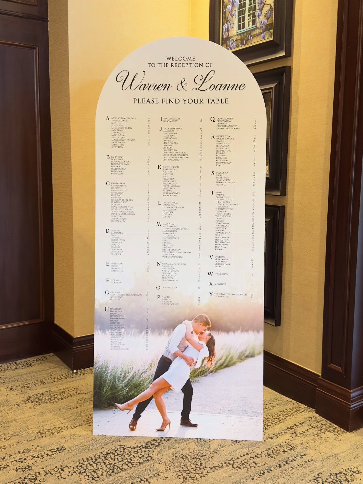 Arched wedding seating chart with guest names and a photo of a couple kissing.