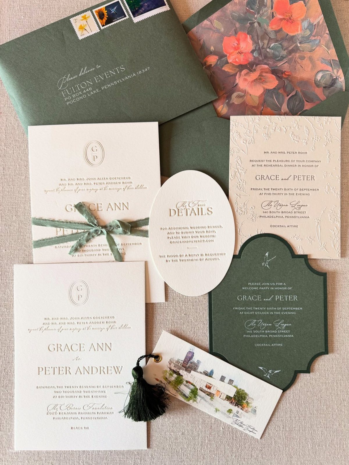 Wedding invitation suite with green envelopes, white cards, and floral accents on fabric.