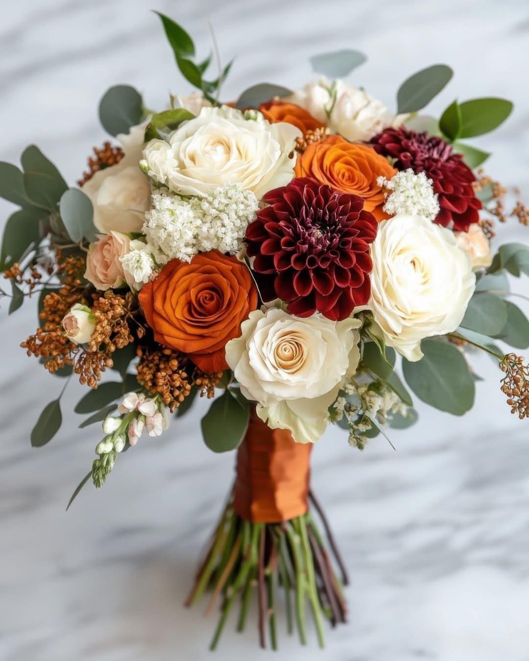Bridal bouquet with white, orange, and burgundy flowers tied with orange ribbon.