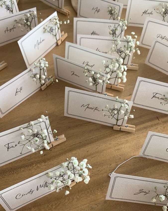 White wedding place cards with cursive names and baby's breath on wooden clips.