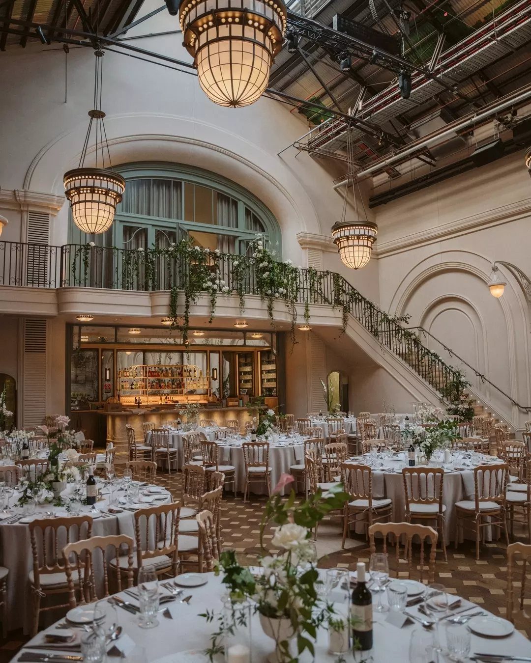 Grand wedding venue featuring round dining tables and a staircase decorated with greenery.