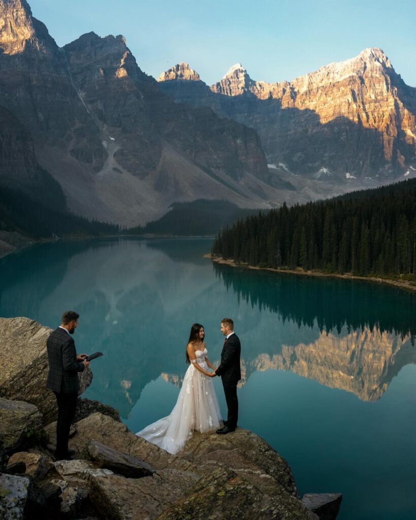 Bride and groom holding hands during a wedding ceremony overlooking a mountain lake.