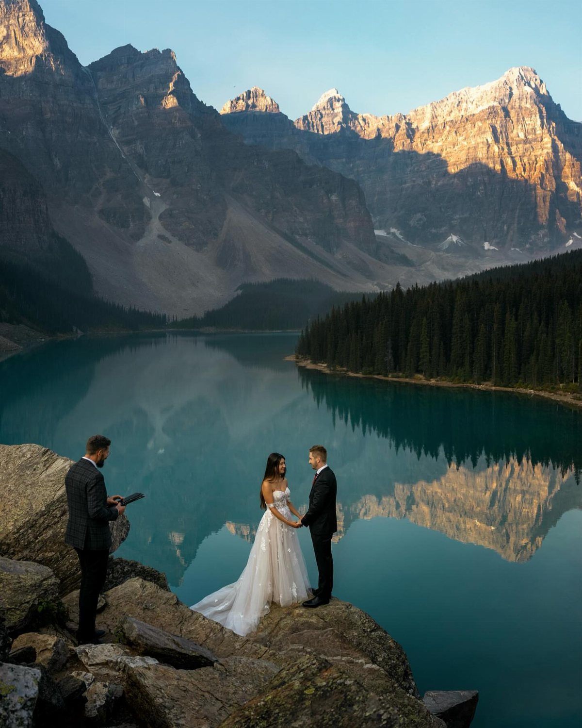 Bride and groom holding hands during a wedding ceremony overlooking a mountain lake.