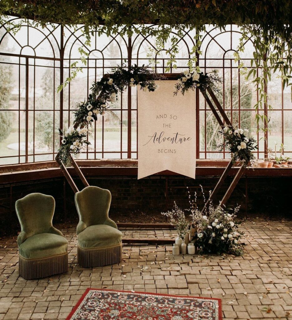 Hexagonal wooden wedding arch adorned with evergreen branches and white floral arrangements.