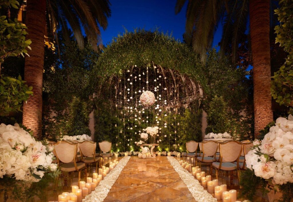 Outdoor wedding ceremony setup with a floral arch, candlelit aisle, and white chairs.